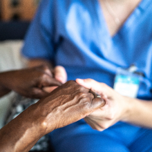 A closeup of a woman in scrubs holding the hands of an older person